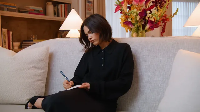 Ariana Greenblatt sitting on a sofa in a dark outfit.