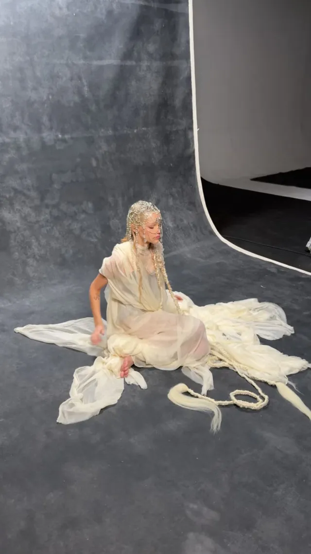 Grace VanderWaal sitting barefoot amid fabric on a studio floor.