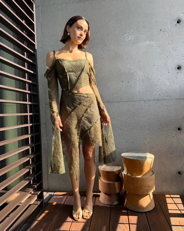 Camila Mendes standing on a balcony in a patterned outfit and gold heels.