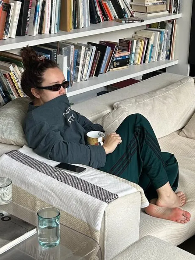 Olivia Cooke relaxing on a sofa beside bookshelves.