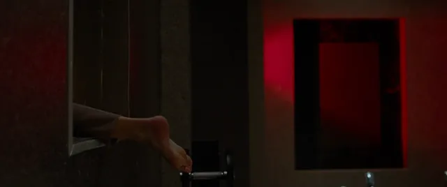 Maika Monroe lying barefoot in a dimly lit room in a scene.