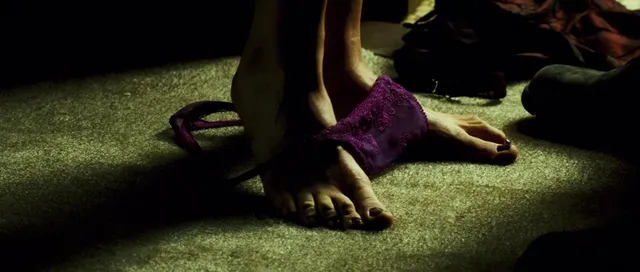 Monica Bellucci a dimly lit screen detail of bare feet beside slippers.