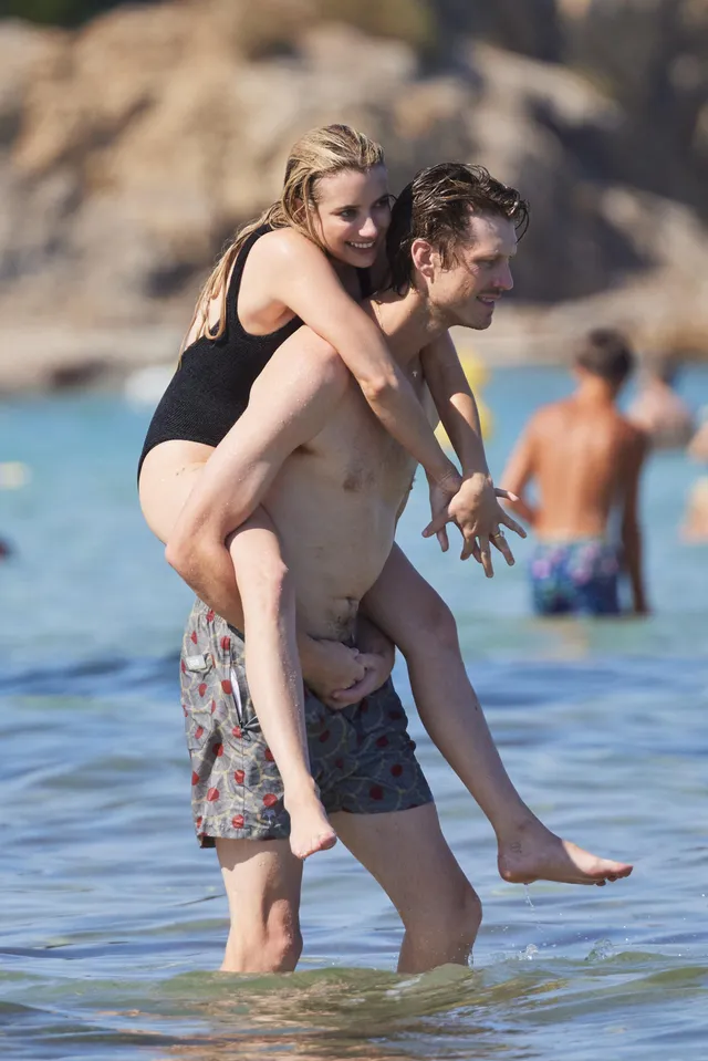 Emma Roberts riding on a man's back while barefoot at the beach.