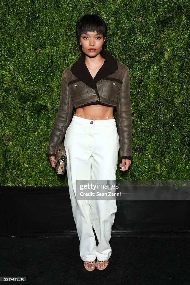 Whitney Peak wearing white trousers, a brown cropped jacket and heels at an event.