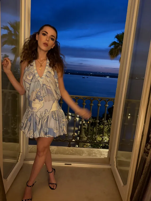 Kiernan Shipka standing in a doorway in a patterned dress and black heels.