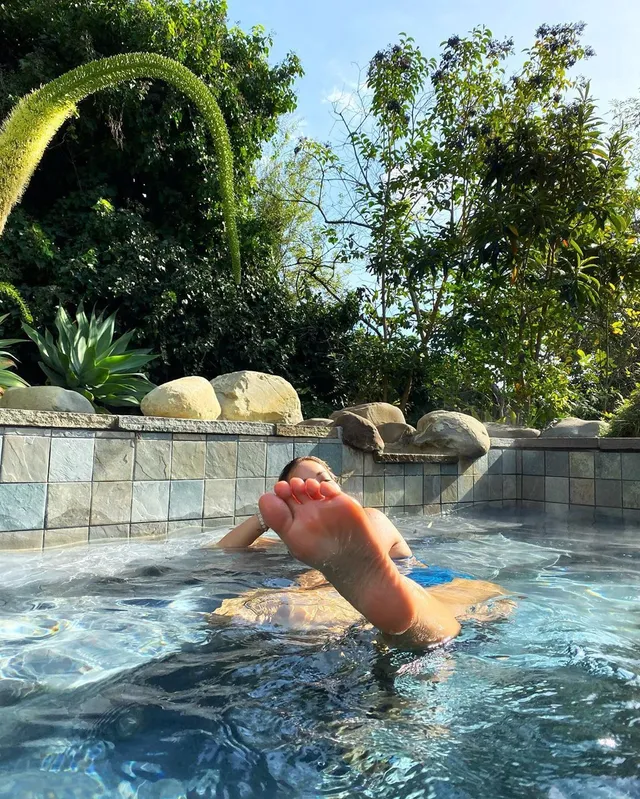 Rita Ora raising bare soles from a pool.
