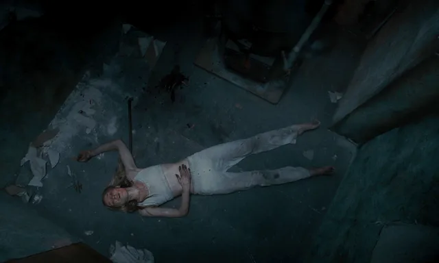Sophie Turner a dimly lit overhead screen scene in a pale outfit.