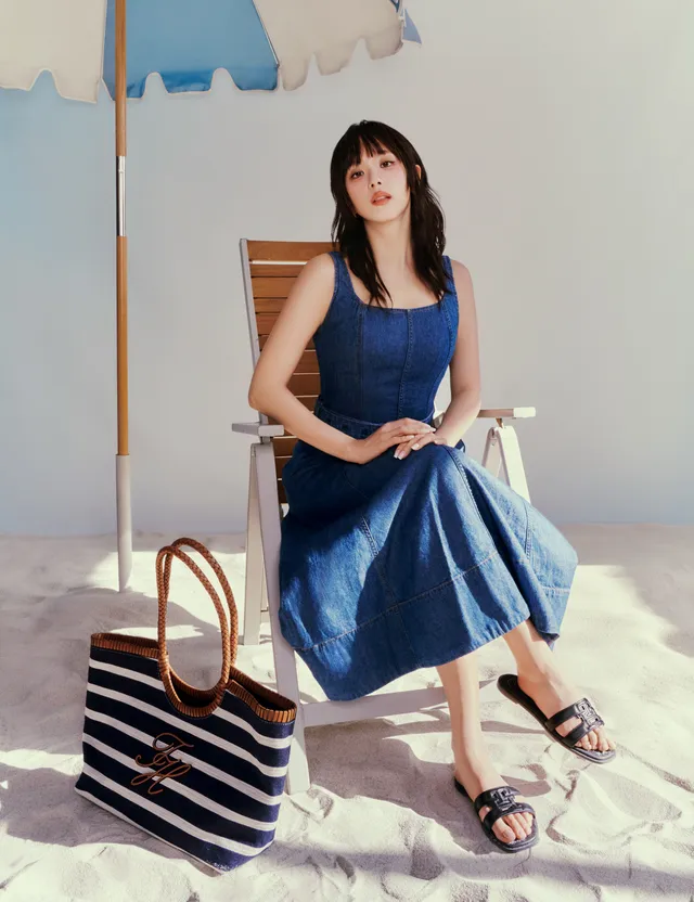 Jisoo sitting on a beach chair in black flat slides and a blue dress.