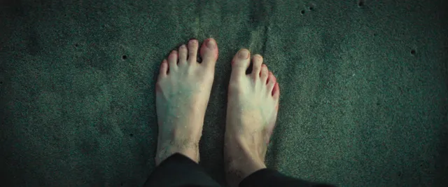 Anya Taylor-Joy standing barefoot on a dark floor.