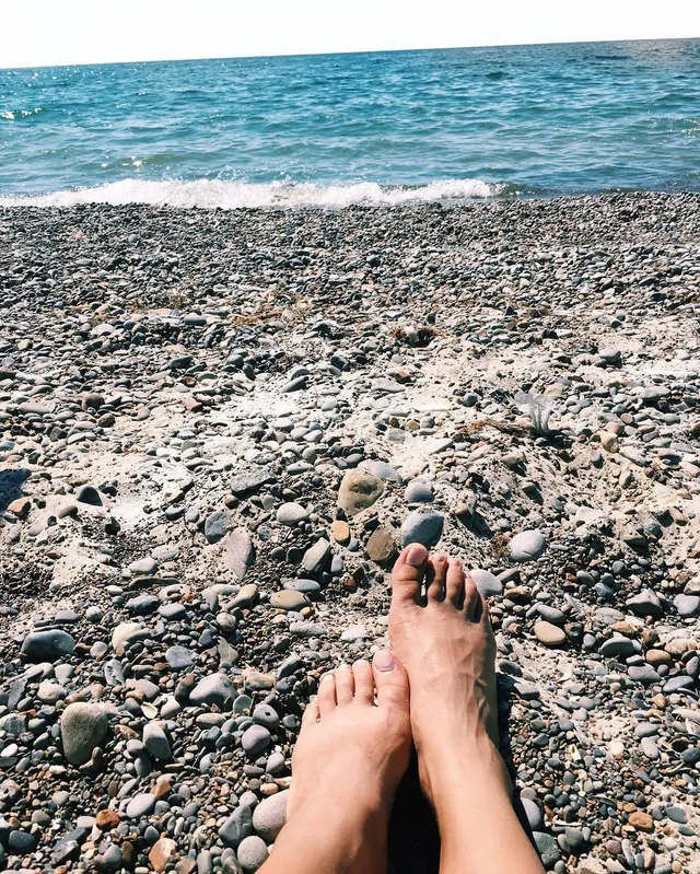 Kiana Madeira shown with bare feet resting on a pebbled beach.