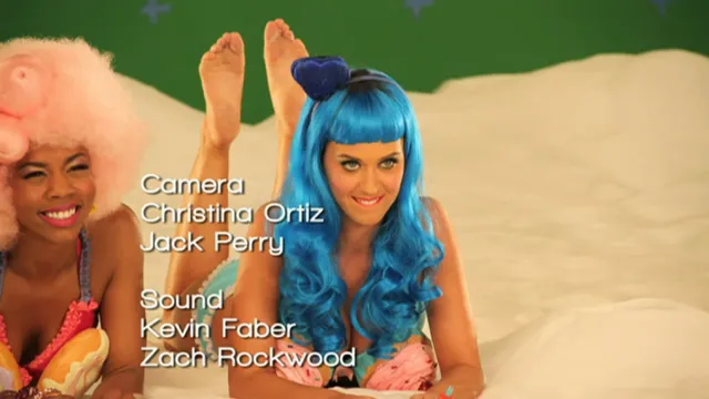 Katy Perry posing barefoot on a bed with feet raised behind her.