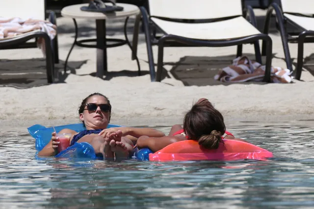 Alex Morgan relaxing barefoot on a pool float beside a companion.