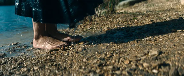Tessa Thompson standing by a stony shoreline in a screen scene.