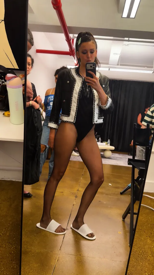 Nina Dobrev posing beside a mirror wearing white flat slides.