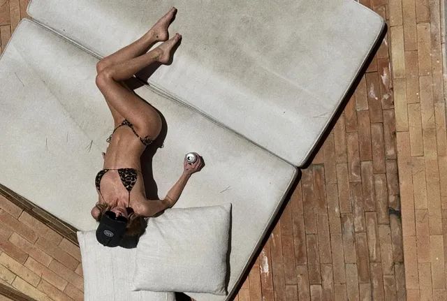 Samara Weaving reclining barefoot on a pale sofa beside a pool.