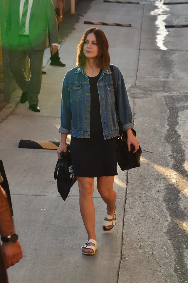 Melissa Benoist wearing a denim jacket and white heeled sandals outdoors.