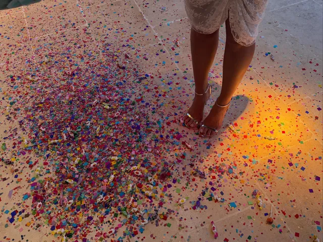 Dua Lipa standing barefoot on a floor covered in confetti.