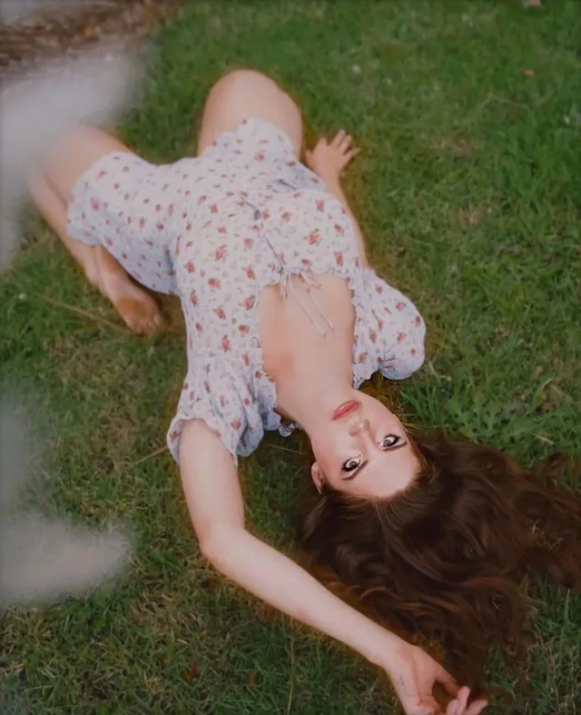 Lana Del Rey lying barefoot on grass in a floral dress.