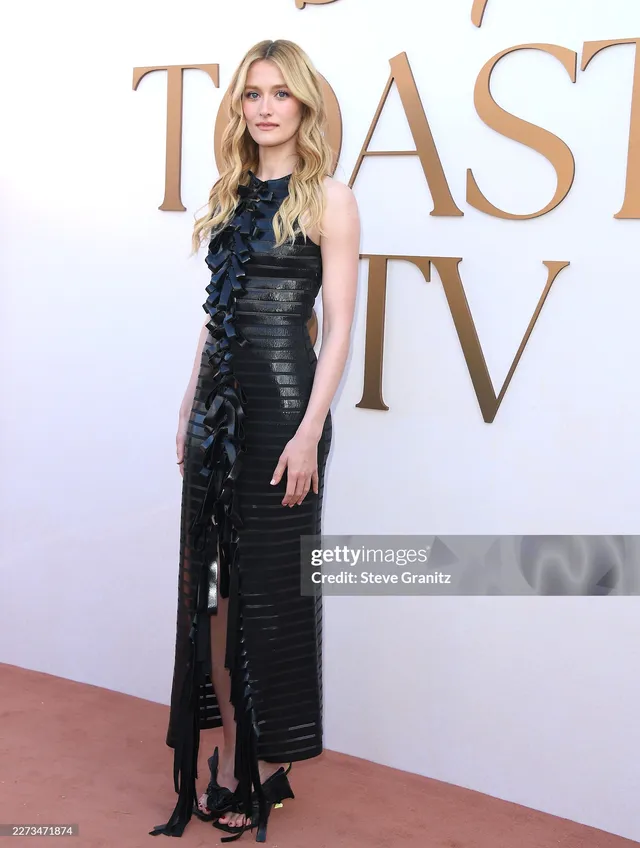 Sarah Pidgeon posing on a red carpet in a long black dress and heels.