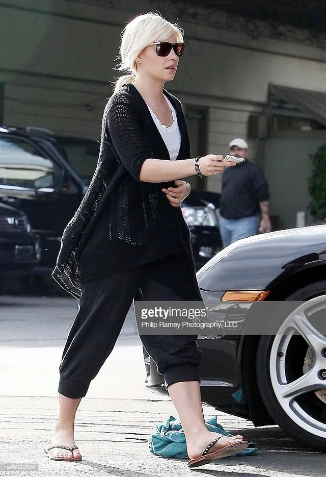 Elisha Cuthbert walking beside a car in cropped trousers and flip-flops.