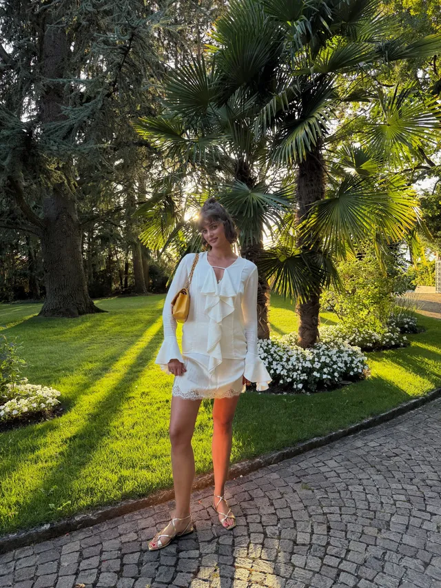 Taylor Hill standing in flat sandals on a garden path wearing a white outfit.
