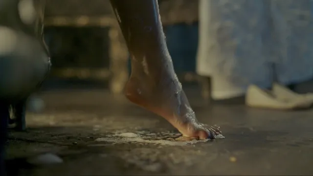 Freya Allan stepping barefoot on an indoor floor in a film scene.