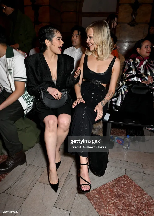 Grace VanderWaal sitting beside another person at an event in black heels.