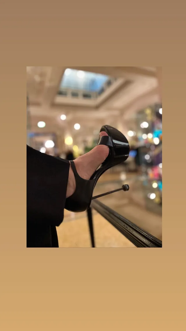 Hayley Atwell showing black pumps while seated indoors.