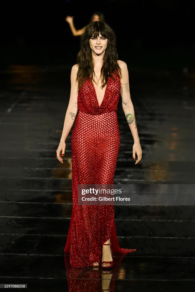 Cara Delevingne posing at a premiere in a long red dress.