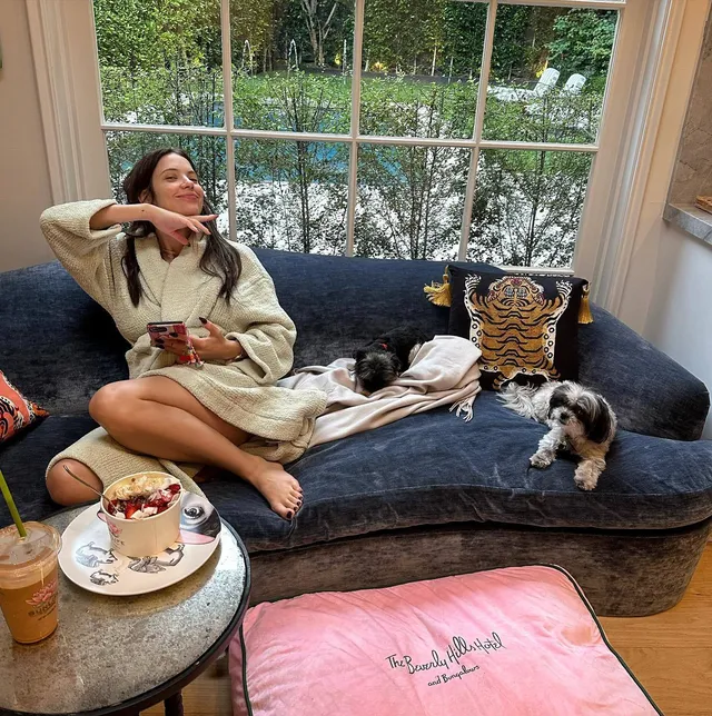 Ashley Benson sitting cross-legged on a sofa beside a dog.