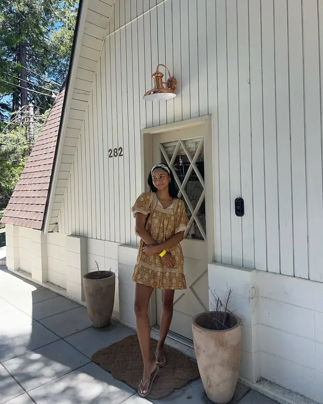 Greta Onieogou standing by a doorway in a yellow patterned dress and flats.