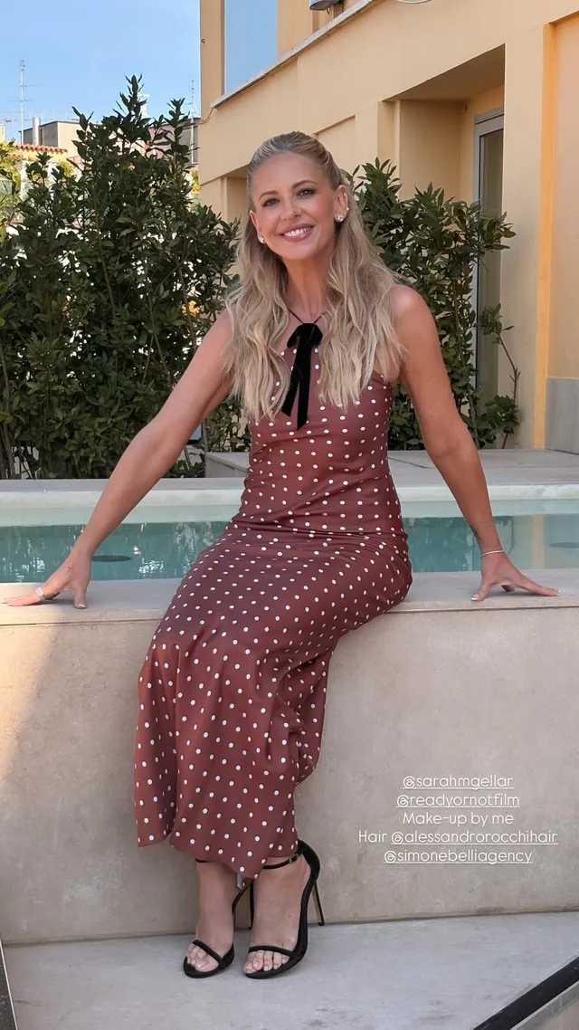 Sarah Michelle Gellar sitting outdoors in a patterned dress and black heels.