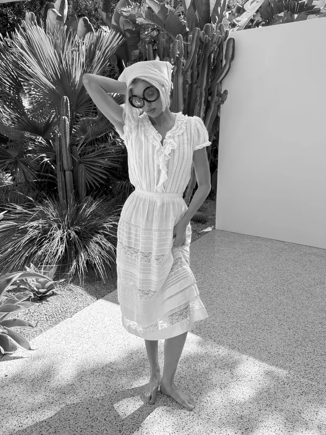 Elsa Hosk standing barefoot in a garden wearing a white dress.