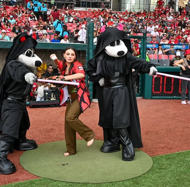 Dafne Keen standing barefoot beside baseball mascots on the field.