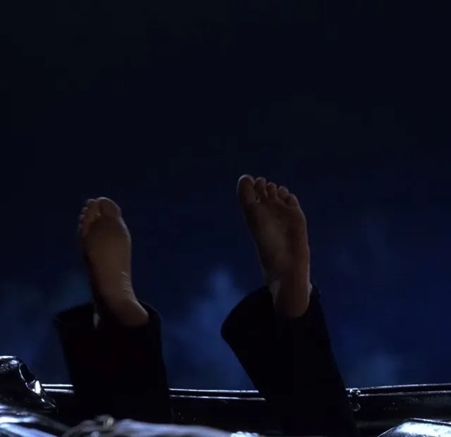Anne Hathaway raising bare soles in a dark screen scene.
