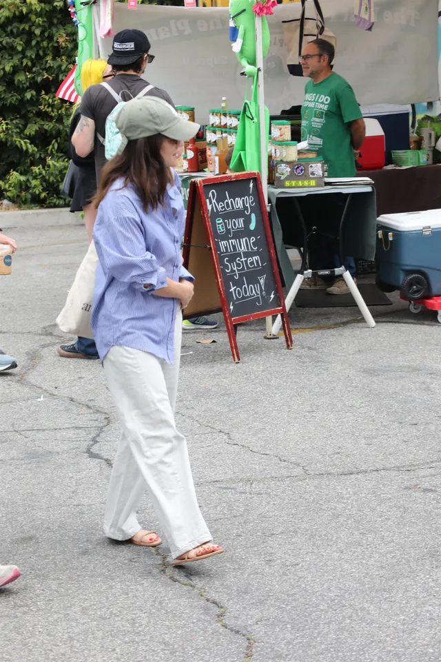 Lucy Hale walking beside a market stall in a blue shirt and flip-flops.