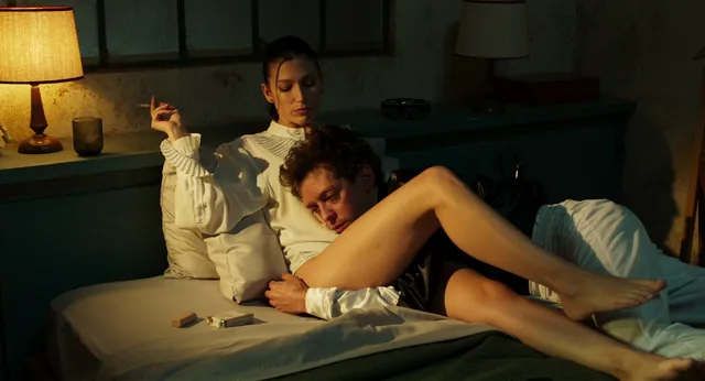 Úrsula Corberó lying barefoot on a bed with a fellow performer in a scene.
