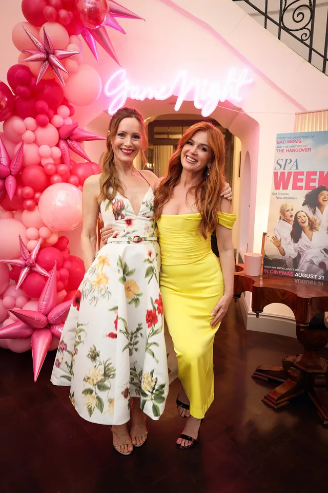 Isla Fisher posing with a companion beside a pink event display.