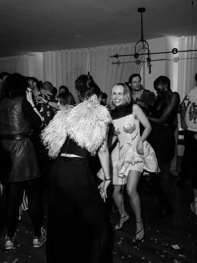 Emilia Clarke dancing in a pale dress and heels at an indoor party.