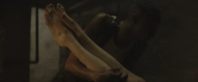 Margaret Qualley a dimly lit screen portrait with bare feet raised.