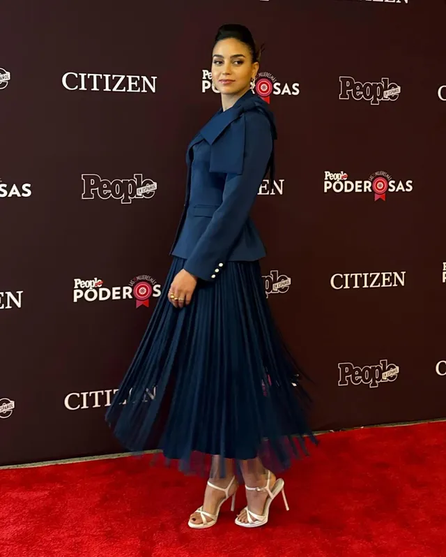 Melissa Barrera posing in a blue dress and metallic heels at an event.