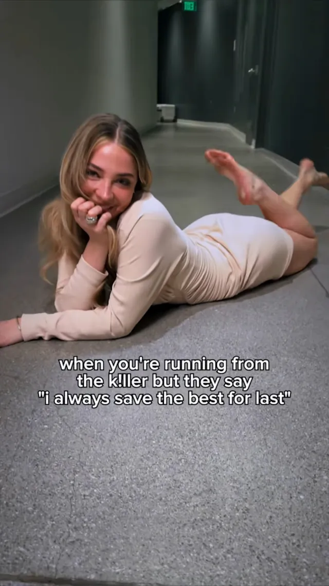 Madelyn Cline lying barefoot on a corridor floor and smiling.