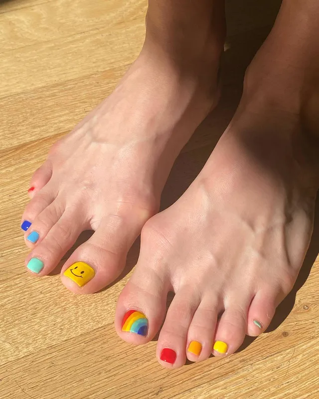 Chloë Grace Moretz showing multicolored toenail polish on a wooden floor.