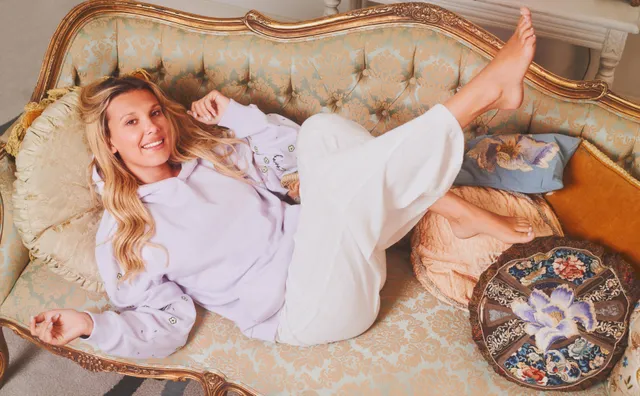 Millie Bobby Brown lying on an ornate sofa in a white dress.