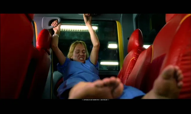Uma Thurman reclining barefoot in a blue outfit in a film scene.