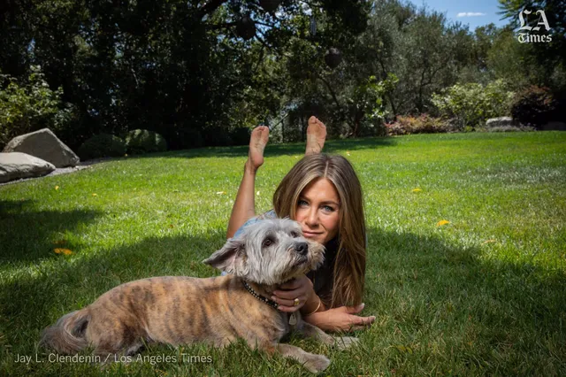 Jennifer Aniston lying barefoot on the grass beside a dog.