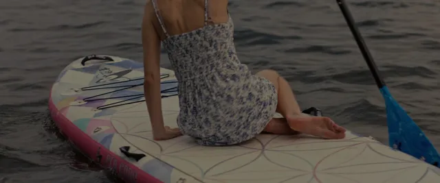 Anna Kendrick kneeling barefoot beside a blue paddle on a paddleboard.