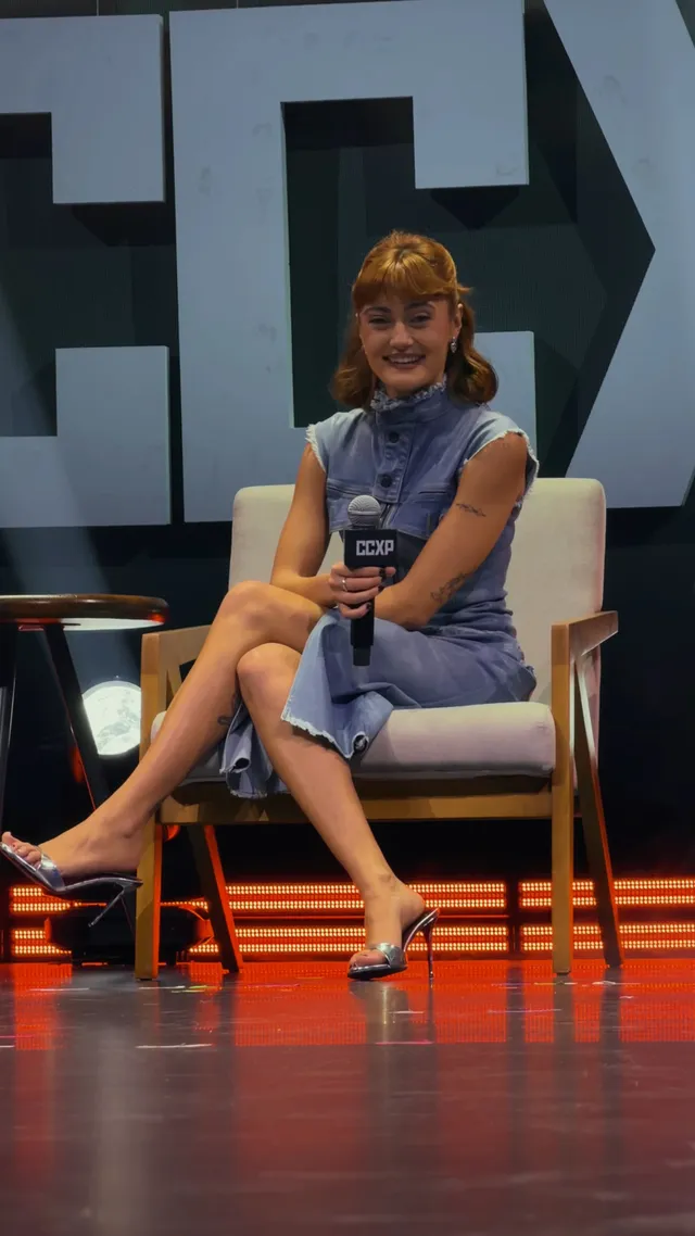 Ella Purnell sitting onstage in a blue dress and metallic sandals.