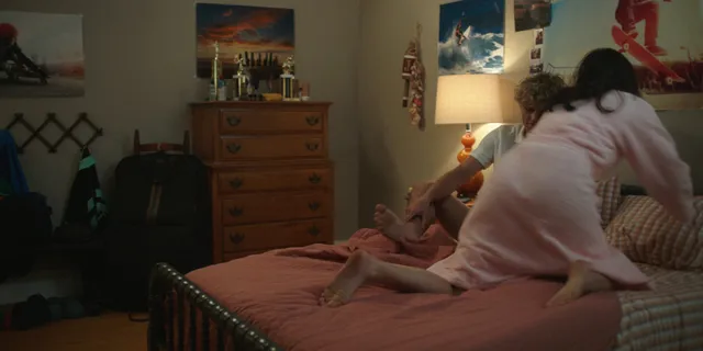 Lola Tung sitting on a bed in a pale top in a screen capture.