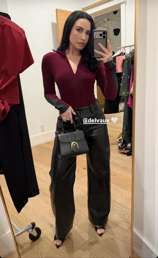 Demi Lovato posing for a mirror photograph in dark trousers and heels.